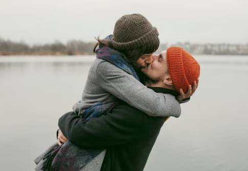 Couple kissing by lake wearing colorful hats